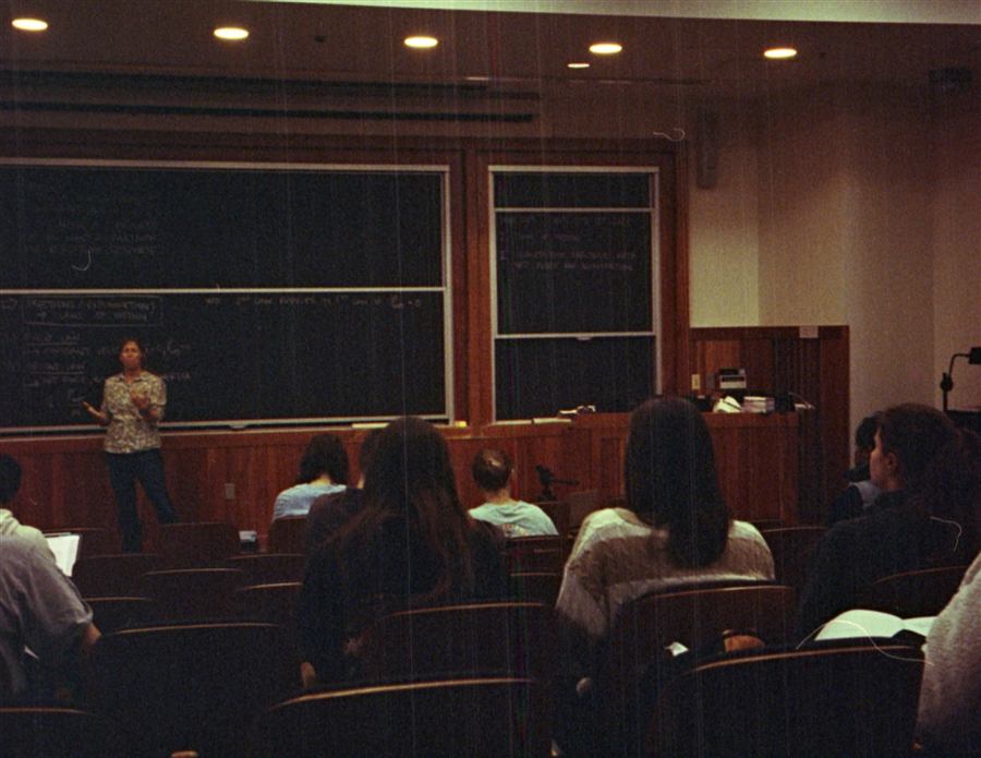 Amphithéâtre universitaire avec un enseignant devant un tableau noir et des étudiants au premier plan.