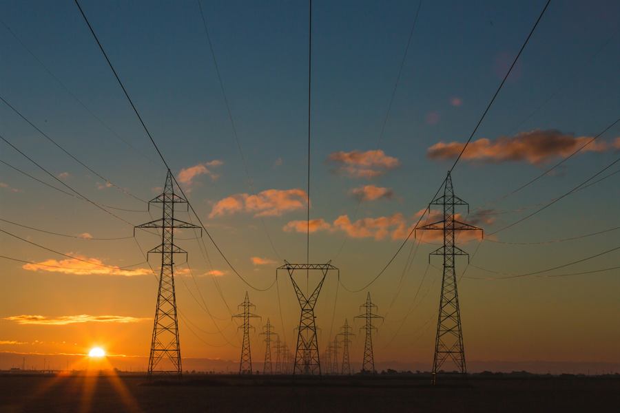 Pylônes électriques à haute tension au coucher du soleil, représentant le secteur de l'énergie.